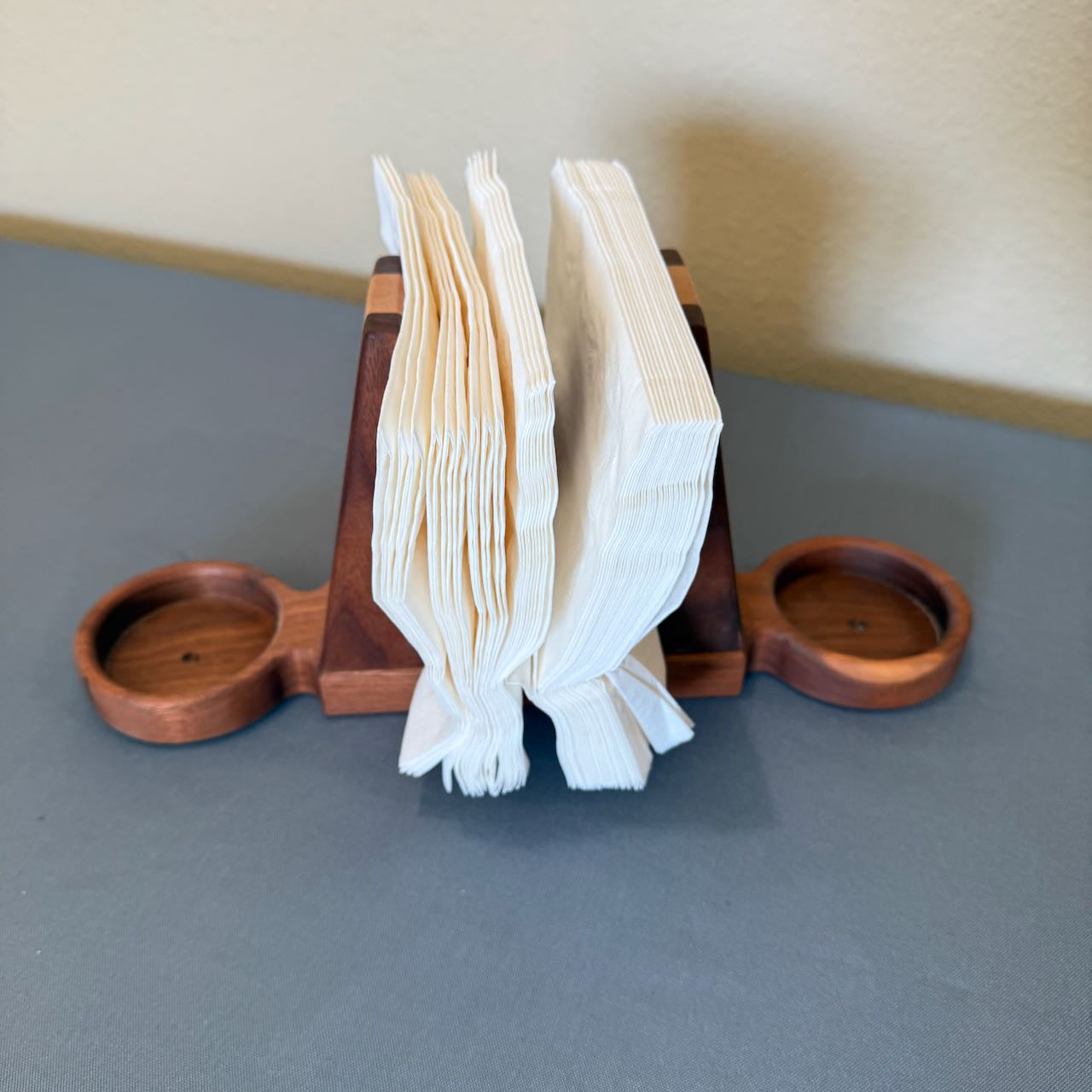 Wooden bookend style napkin holder with napkins and salt and pepper trays on each end on a gray background.
