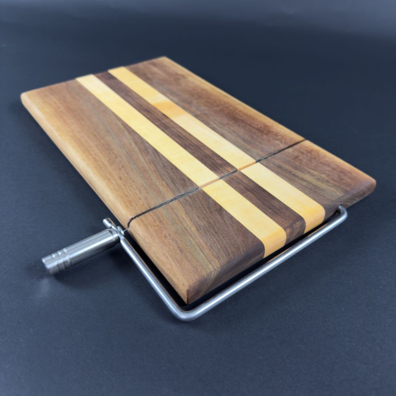 Wooden cheese cutting board with metal handle on a dark background