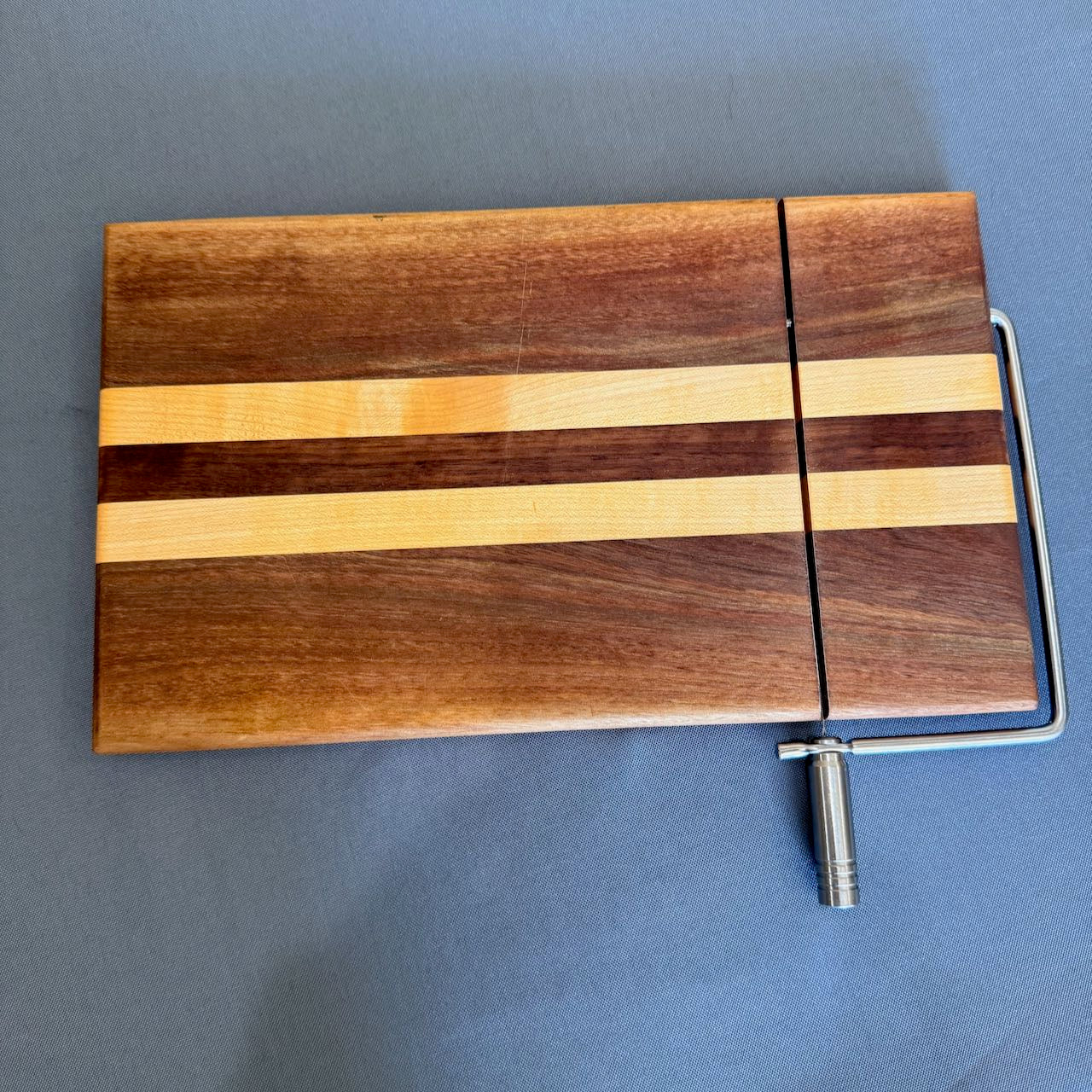 Cheese cutting board shown from a top view. Chrome finish cutting handle and arm. Colorful linear pattern of walnut and maple. Measure a generous 8 x 13. Extra cutting wires included. Please contact me for additional assistance.