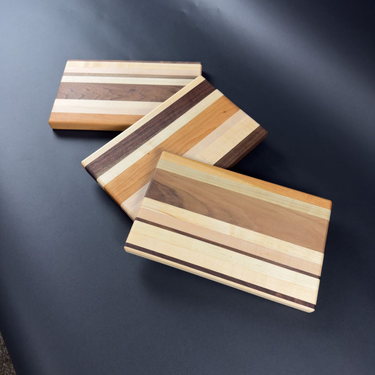 Three compact hardwood chopping boards with striped patterns on a dark surface. Showing each with different patterns.