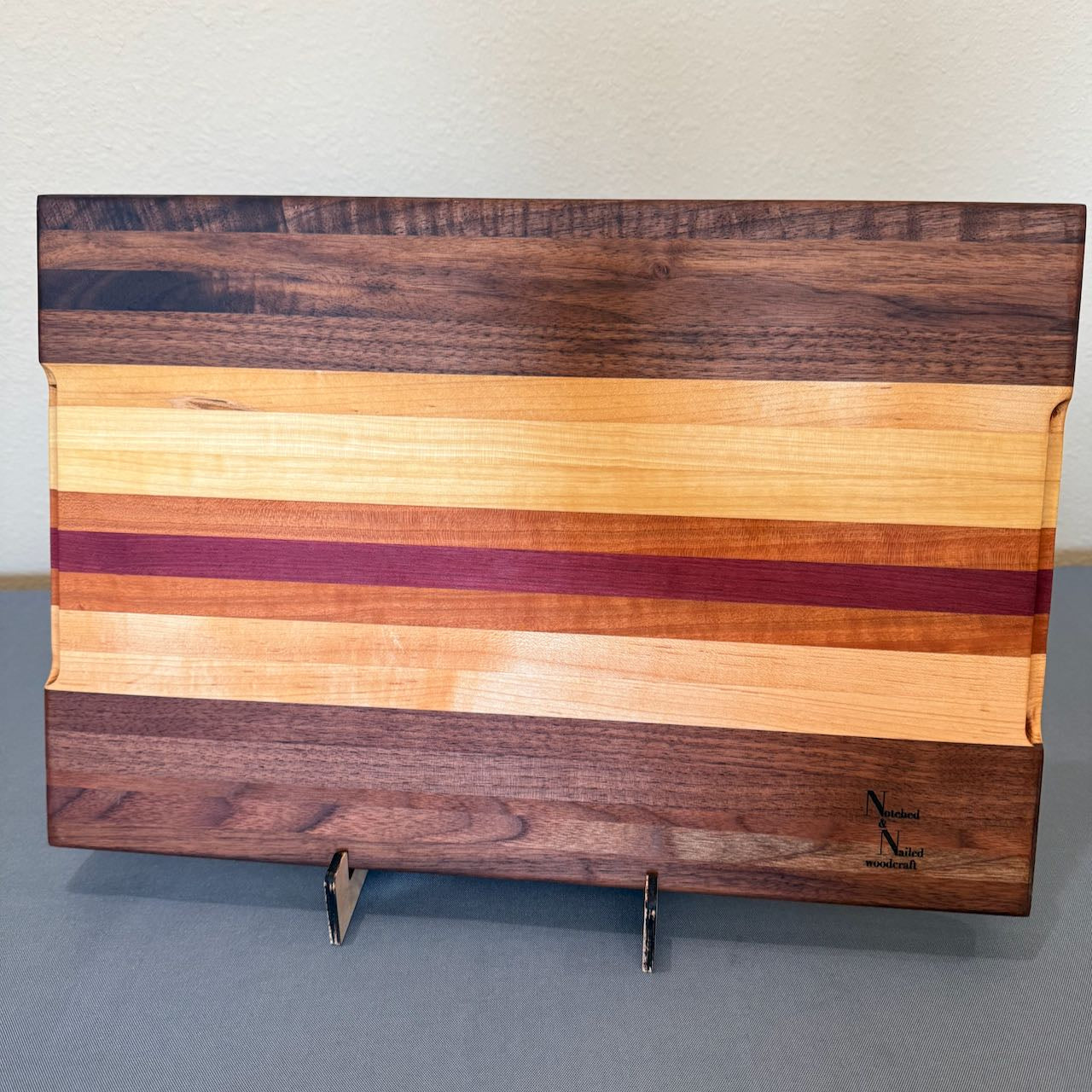 Beautiful solid hardwood cutting board with juice groove and finger holds for easy lifting. Made from walnut, cherry, maple and purple heart. 12 x 18 1.25, viewed standing on edge bottom side.