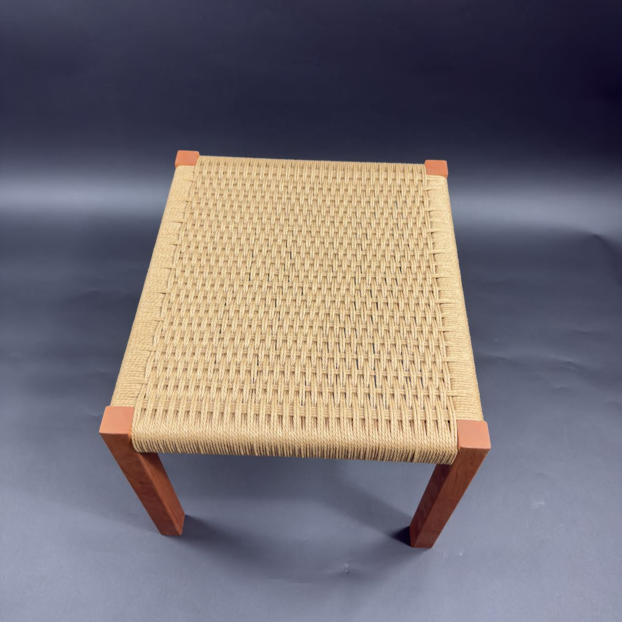 Beautiful  square cherry wood foot stool with danish cord weave seating, top view on a dark background. 16 x 16 and 17 inches high