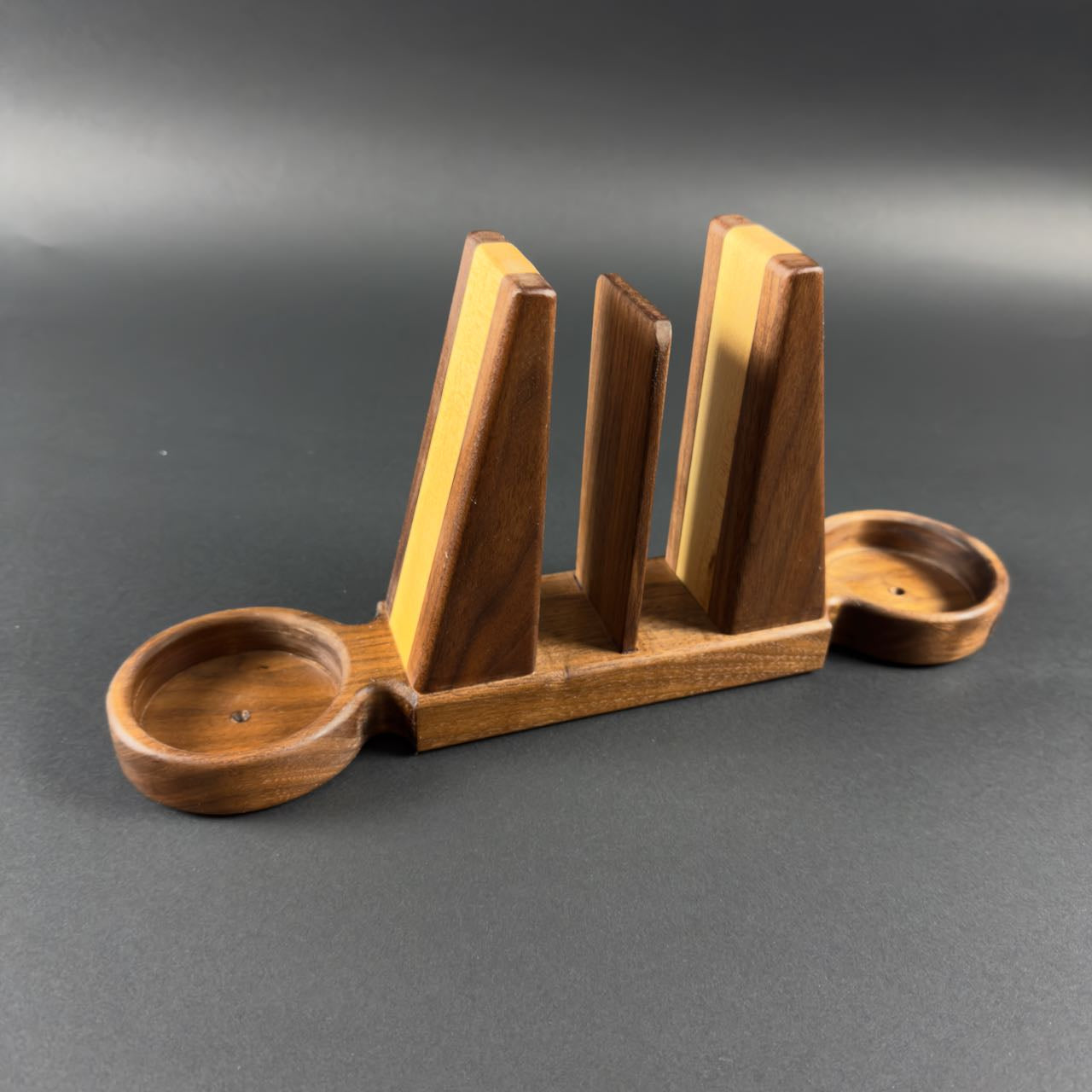 Wooden bookend style napkin holder with salt and pepper trays on each end on a gray background.