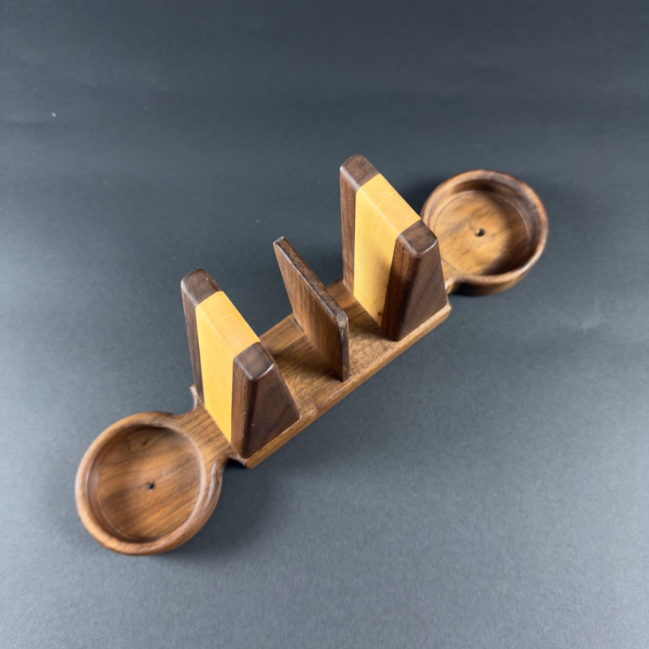 Wooden bookend style napkin holder with salt and pepper trays on each end on a gray background.