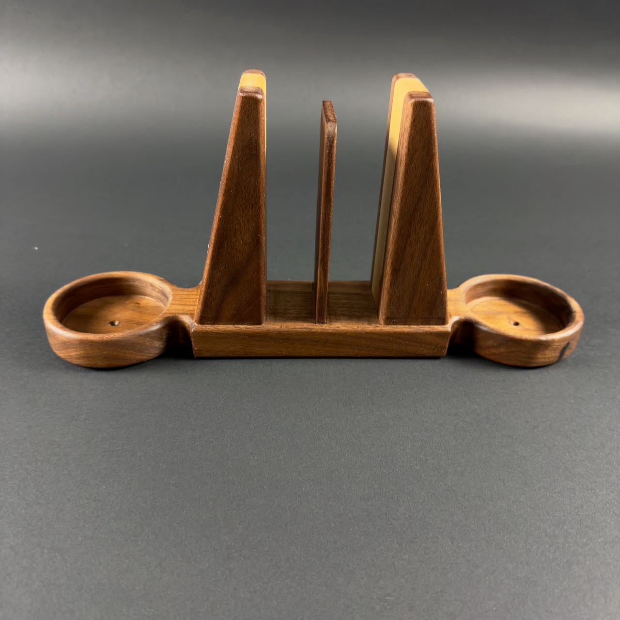 Wooden bookend style napkin holder with salt and pepper trays on each end on a gray background.