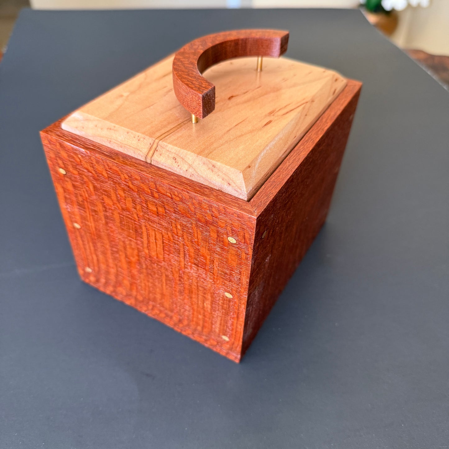 Beautifully crafted keepsake box.  Corner view. The body is make of leopard wood with an ambrosia maple top. The handle is a crescent moon shape standing on three thin brass posts.  Small brass accents adorn the corners. It measures 6 x5 and 6 1/2 inches tall. For additional help please reach out to me.