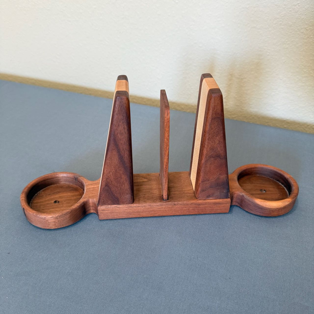 Wooden bookend style napkin holder with salt and pepper trays on each end on a gray background. Side view.
